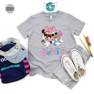 May include: A gray t-shirt with a graphic of Minnie Mouse and Daisy Duck wearing sunglasses and holding ice cream cones. The text "Bestie" is printed below the graphic in pink and blue letters.
