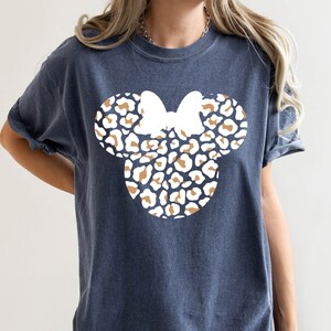 Peut inclure: Un t-shirt bleu fonc&eacute; avec un motif de t&ecirc;te de Minnie Mouse en imprim&eacute; l&eacute;opard blanc et marron.