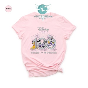 May include: Pink t-shirt with a graphic of Mickey Mouse, Minnie Mouse, Donald Duck, and Goofy celebrating Disney's 100th anniversary. The graphic includes the text "Disney" and "100 Years of Wonder".