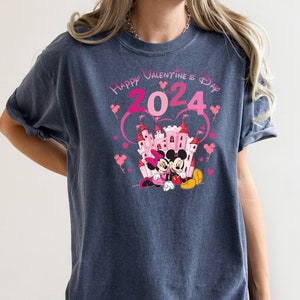 May include: A dark blue t-shirt with a pink and white graphic of Mickey and Minnie Mouse in front of a pink castle. The graphic also includes the text "Happy Valentine's Day 2024" in pink.