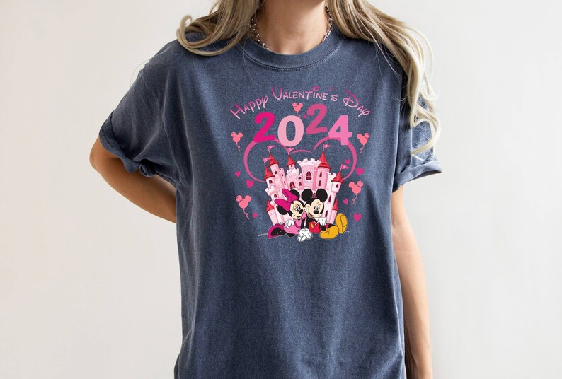 May include: A dark blue t-shirt with a pink and white graphic of Mickey and Minnie Mouse in front of a pink castle. The graphic also includes the text "Happy Valentine's Day 2024" in pink.