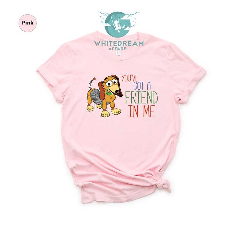 Op de afbeelding: Roze T-shirt met een cartoon afbeelding van een hond uit de Toy Story-filmfranchise. De tekst "You've Got a Friend in Me" staat op het shirt gedrukt.