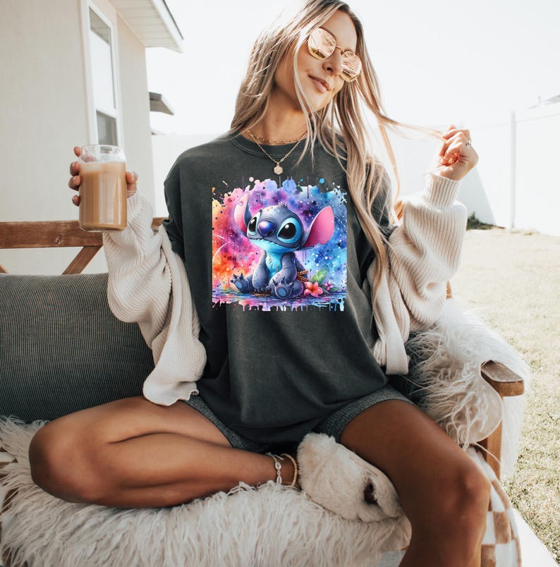 Pu&ograve; includere: Felpa grigio scuro con un'illustrazione ad acquerello del personaggio Stitch di Lilo & Stitch. L'opera presenta Stitch con uno sfondo colorato a spruzzi. La felpa &egrave; uno stile casual e confortevole.