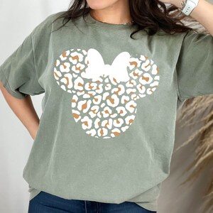 Peut inclure: Un t-shirt vert avec un motif de t&ecirc;te de Minnie Mouse en imprim&eacute; l&eacute;opard blanc et marron.