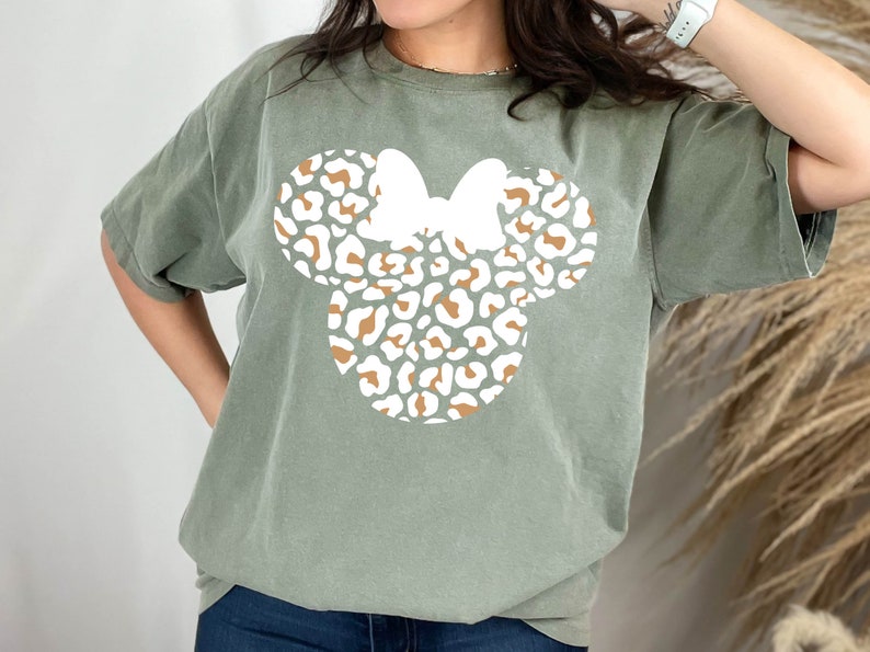Peut inclure: Un t-shirt vert avec un motif de t&ecirc;te de Minnie Mouse en imprim&eacute; l&eacute;opard blanc et marron.