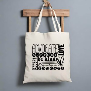 K&ouml;nnte beinhalten: Eine wei&szlig;e Stofftasche mit schwarzem Text, der "Advocate, Support, Be Kind, Love, Educate" lautet. Der Text ist kreisf&ouml;rmig mit einem Herzsymbol angeordnet.