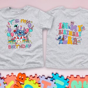 Puede incluir: Camiseta gris con un personaje azul Stitch en la parte delantera. La camiseta dice "It's my birthday" en letras de colores. La parte posterior de la camiseta dice "In my birthday era" en letras de colores.