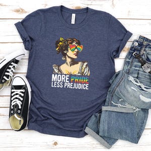 May include: A heather navy blue t-shirt with a graphic of a woman wearing rainbow sunglasses and the text "More Pride Less Prejudice".