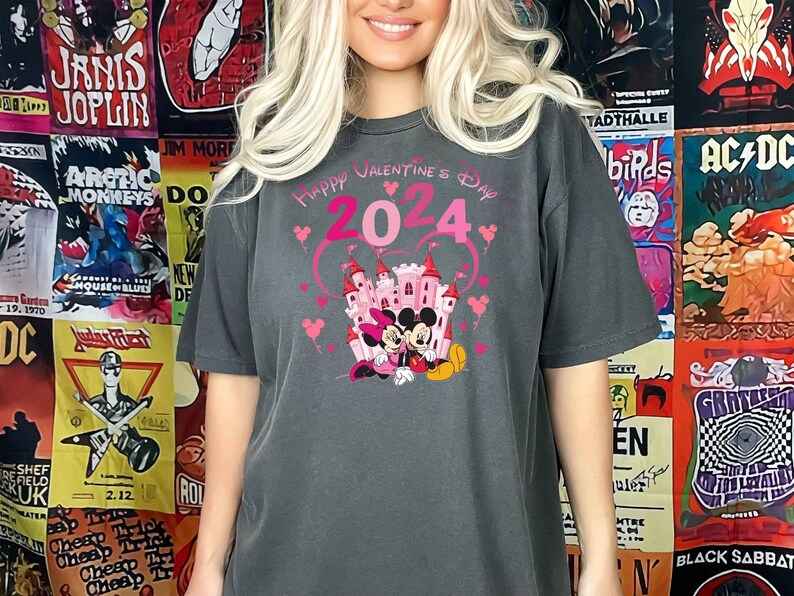 May include: A dark gray t-shirt with a pink graphic of Mickey Mouse and Minnie Mouse in front of a pink castle. The graphic also includes the text "Happy Valentine's Day 2024" in pink.