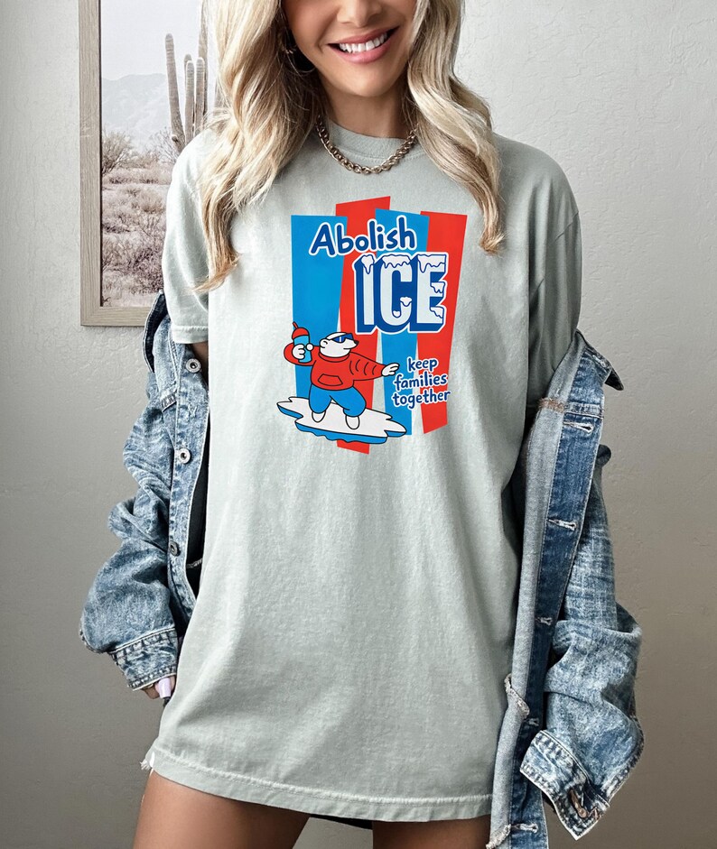May include: A light green t-shirt with the words "Abolish ICE" in blue and red, along with a cartoon character holding a popsicle. The text "keep families together" is also included. The shirt is a casual style.