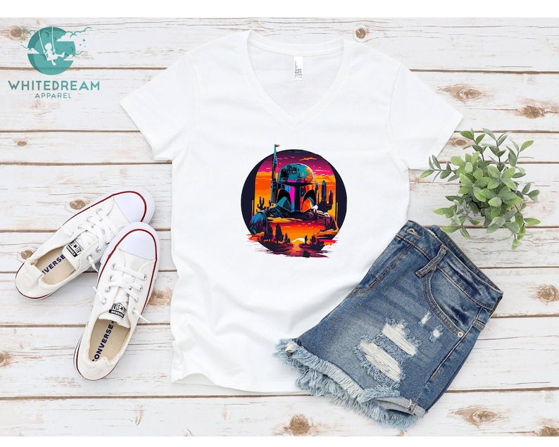 Pu&ograve; includere: Maglietta bianca a collo a V con una grafica di un personaggio di Star Wars, Boba Fett, in una scena di tramonto retr&ograve;. La grafica &egrave; in un cerchio con uno schema di colori rosa, arancione e blu.
