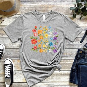 May include: A gray t-shirt with a rainbow floral design. The flowers are in shades of red, orange, yellow, green, blue, and purple.