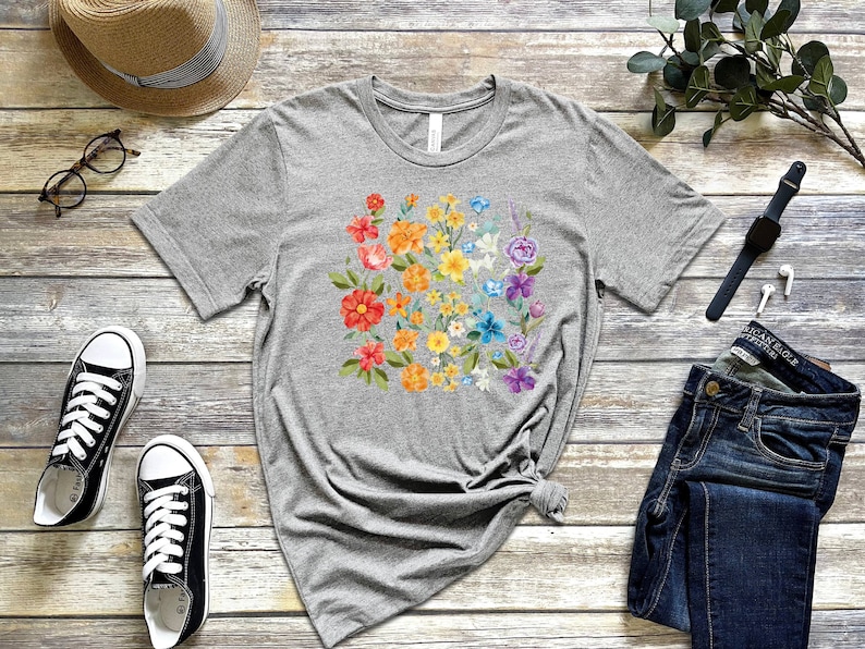 May include: A gray t-shirt with a rainbow floral design. The flowers are in shades of red, orange, yellow, green, blue, and purple.