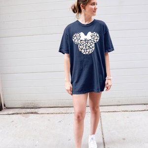 Peut inclure: Un t-shirt bleu marine avec un contour blanc de la t&ecirc;te de Mickey Mouse, rempli d'un motif l&eacute;opard en or et blanc. Le n&oelig;ud sur la t&ecirc;te de Mickey est blanc.