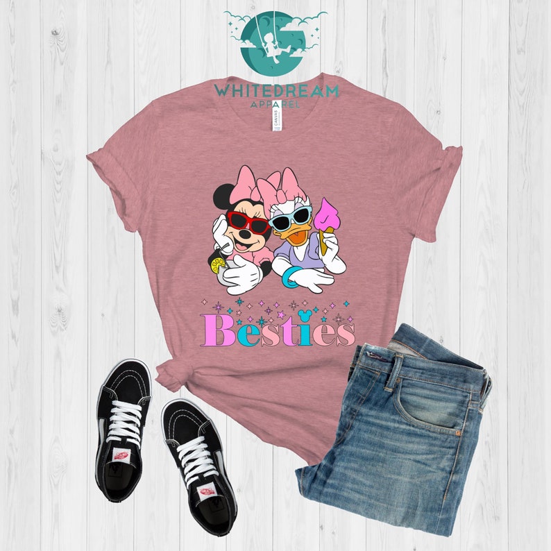 May include: A pink t-shirt with a graphic of Minnie Mouse and Daisy Duck wearing sunglasses and holding ice cream cones. The text "Besties" is printed below the graphic.