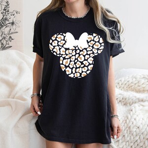 Peut inclure: T-shirt noir avec un motif de t&ecirc;te de Minnie Mouse en imprim&eacute; l&eacute;opard blanc et marron.