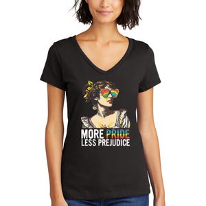 May include: Black v-neck t-shirt with a colorful illustration of a woman wearing rainbow heart-shaped sunglasses. The text "More Pride Less Prejudice" is printed below the illustration.
