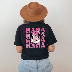 以下が含まれることがあります： 黒地にピンクと白のミニーマウスのグラフィックがプリントされたTシャツ。"MAMA"という文字が4回繰り返されている。