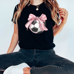 May include: Black t-shirt with a pink bow tied around a soccer ball.