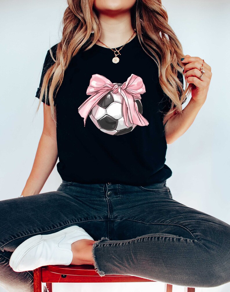 May include: Black t-shirt with a pink bow tied around a soccer ball.