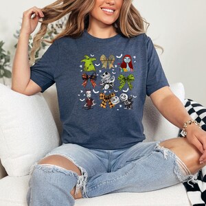 May include: Navy blue t-shirt featuring a colorful graphic of characters and bows from The Nightmare Before Christmas. The design includes images of Sally, Jack Skellington, and Oogie Boogie. The shirt is a crew neck and has short sleeves.