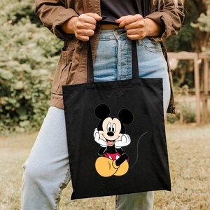 K&ouml;nnte beinhalten: Schwarze Tragetasche mit einem Cartoon-Bild von Mickey Mouse in einem roten und gelben Outfit. Mickey Mouse sitzt mit den H&auml;nden am Kinn und hat ein breites L&auml;cheln.