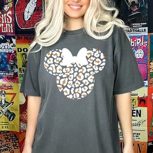 Peut inclure: Un t-shirt gris fonc&eacute; avec un motif de t&ecirc;te de Minnie Mouse en imprim&eacute; l&eacute;opard brun et blanc.