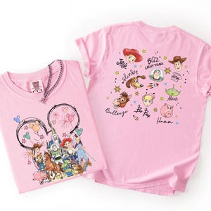 May include: Two pink t-shirts featuring Disney characters. One shirt displays a Mickey Mouse outline with fireworks and Disney characters. The other shirt showcases various Toy Story characters with their names. Both shirts are made of soft material.