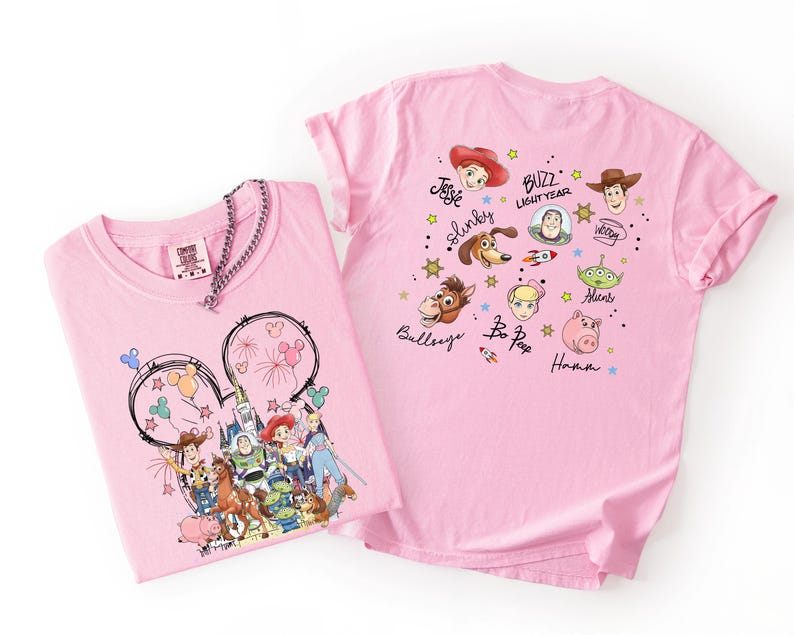 May include: Two pink t-shirts featuring Disney characters. One shirt displays a Mickey Mouse outline with fireworks and Disney characters. The other shirt showcases various Toy Story characters with their names. Both shirts are made of soft material.