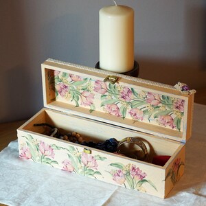 May include: A rectangular wooden box with a floral design on the lid and inside. The box is open and contains jewelry and other small items.