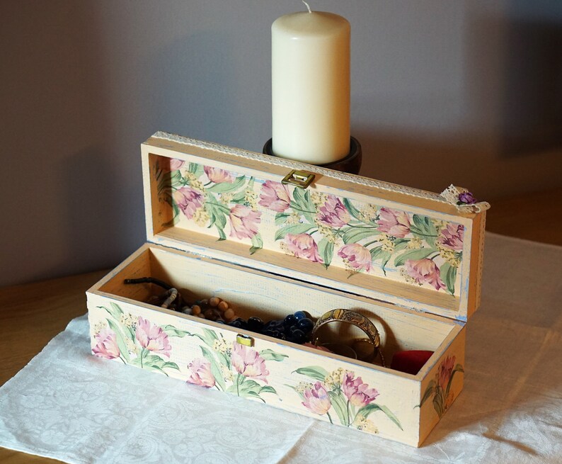 May include: A rectangular wooden box with a floral design on the lid and inside. The box is open and contains jewelry and other small items.