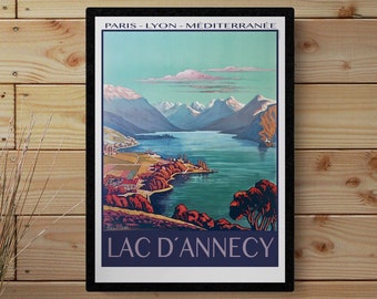 May include: Framed vintage travel poster for Lac d'Annecy, France. The poster shows a scenic view of the lake and mountains, with text at the top and bottom. The colour palette includes blues, greens, and earth tones.