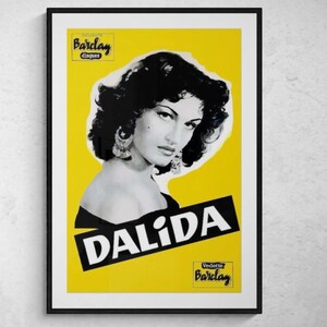 May include: A framed poster featuring a black and white portrait of Dalida against a yellow background. The poster includes the text "DALIDA" in bold white letters on a black diagonal banner, with "Barclay" branding.