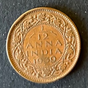 Puede incluir: Una moneda de 1/2 Anna de cobre de la India, fechada en 1930. La moneda presenta un diseño floral alrededor del borde y el texto "1/2 ANNA INDIA 1930" en el centro.