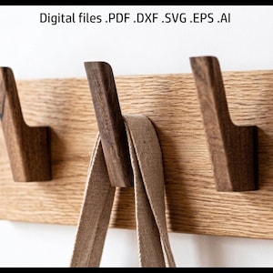 Könnte beinhalten: Wandgarderobe aus Holz mit drei dunkelbraunen Haken. Ein hellbrauner Canvas-Gurt hängt am mittleren Haken. Das Gestell ist aus hellem Holz gefertigt. Der Text oben lautet "Digital files .PDF .DXF .SVG .EPS .AI".