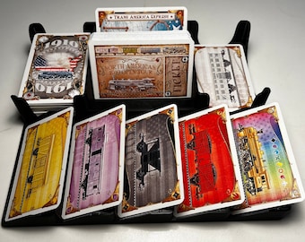 May include: A set of cards for a board game, featuring a train theme. The cards are arranged in a holder, with the top card showing a train with the text "North American 1910 Open Tour".