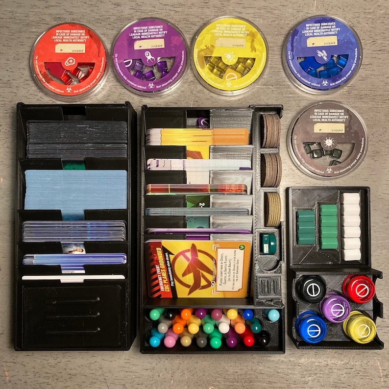 May include: A black organizer with multiple compartments for storing game pieces and cards. The organizer has a compartment for markers, a compartment for small tokens, and a compartment for cards. The organizer is labeled "Emergency Event: CoC Planes Grounded".
