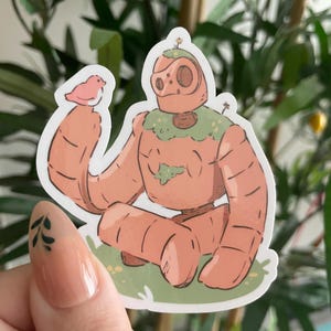 May include: A sticker featuring a cartoon robot with a carrot-like body, seated on green grass. The robot has a round head and is holding a small pink bird. The robot has a green collar and a small flower on its head.