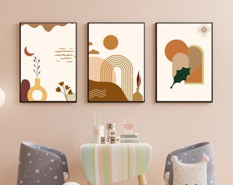 May include: Three abstract art prints with a minimalist design featuring geometric shapes, arches, and sun and moon symbols in shades of brown, orange, yellow, and green. The prints are hung on a light pink wall above a small wooden table with a striped tablecloth. Two children's chairs with star-shaped cushions are placed on either side of the table. A white cloud-shaped pillow with a smiling face is on the floor in front of the table.