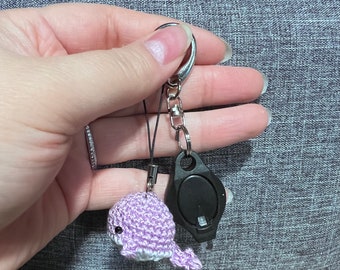 May include: A purple crocheted whale keychain with a black light attached to a silver key ring.