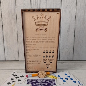 May include: A wooden Five Crowns card game set with a decorative crown logo. Includes a pencil, pegs, and a dealer coin. The set is accompanied by playing cards, with the text "Cards Not Included".