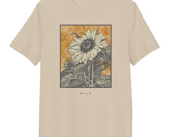 Könnte beinhalten: Beiges T-Shirt mit einer Sonnenblumen-Illustration in einem schwarzen rechteckigen Rahmen. Die Sonnenblume ist in Graustufen vor einem orangefarbenen Hintergrund dargestellt. Das Wort "WILD" ist unten in Schwarz gedruckt.