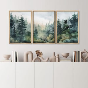 May include: A set of three framed watercolor paintings depicting a misty forest scene with tall, dark green trees. The paintings are arranged in a row on a white wall above a shelf with decorative objects.