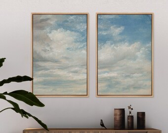 May include: Two framed paintings of a blue sky with white clouds. The paintings are hanging on a white wall above a wooden cabinet.