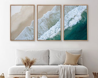 May include: Three framed prints of an aerial view of ocean waves crashing on a sandy beach. The prints are arranged in a row, with the leftmost print showing the beach, the middle print showing the waves, and the rightmost print showing the ocean.