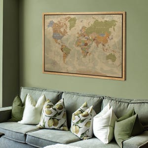 Puede incluir: Un mapa del mundo enmarcado en tonos apagados de verde, marr&oacute;n y beige cuelga de una pared verde. El mapa est&aacute; detallado con contornos y etiquetas de pa&iacute;ses. Debajo del mapa hay un sof&aacute; con cojines decorativos en tonos verdes y blancos.