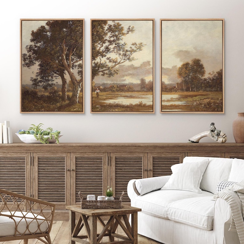 May include: Three framed landscape paintings with a vintage aesthetic. Each features a tree or trees, a body of water, and a muted color palette of browns, greens, and creams. The frames are a light brown color.