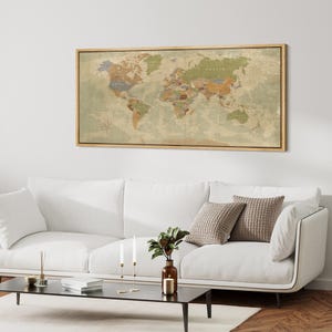 May include: A framed world map with a vintage aesthetic. The map features a neutral color palette with countries in shades of brown, green, and orange. The frame is made of light-colored wood. The map is displayed above a white sofa.