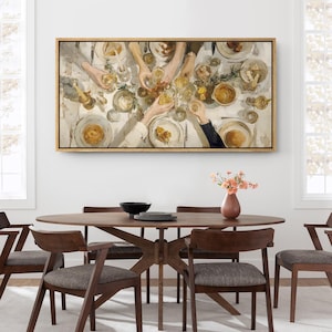 May include: A framed painting depicts a dining scene with hands reaching for glasses and plates. The artwork is in a gold frame, hanging above a wooden dining table with chairs. A vase of flowers sits on the table.