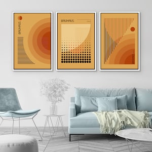 May include: A set of three rectangular wall art prints featuring Bauhaus-inspired geometric designs in shades of orange, yellow, and black. Each print displays abstract patterns, including concentric circles, dots, and vertical lines with the text Bauhaus 1923.